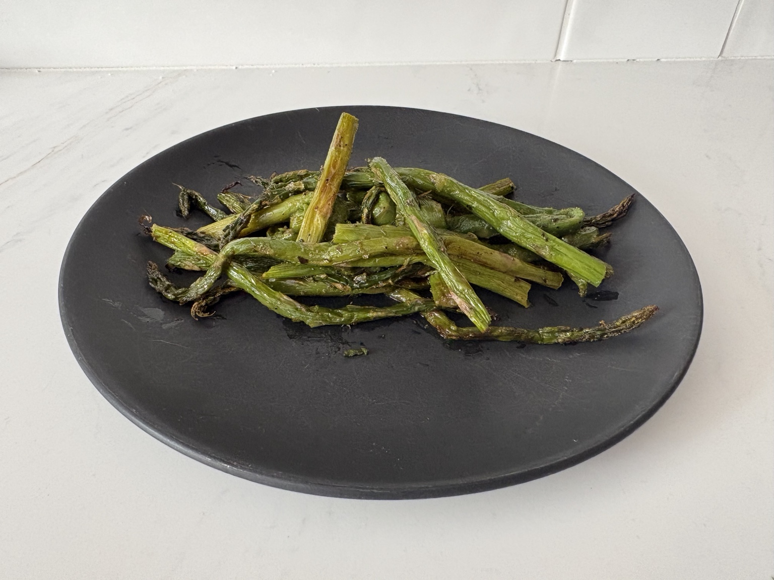 Roasted asparagus with lightly crisped tips on a black plate, viewed from the side