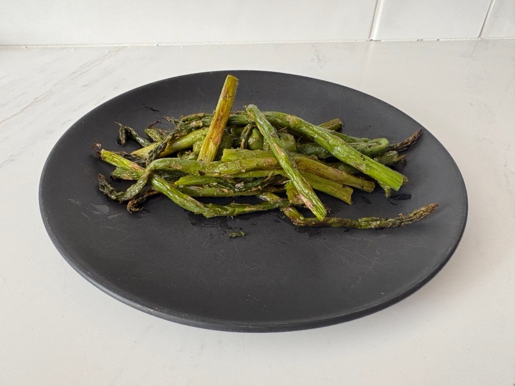 Roasted asparagus with lightly crisped tips on a black plate, viewed from the side