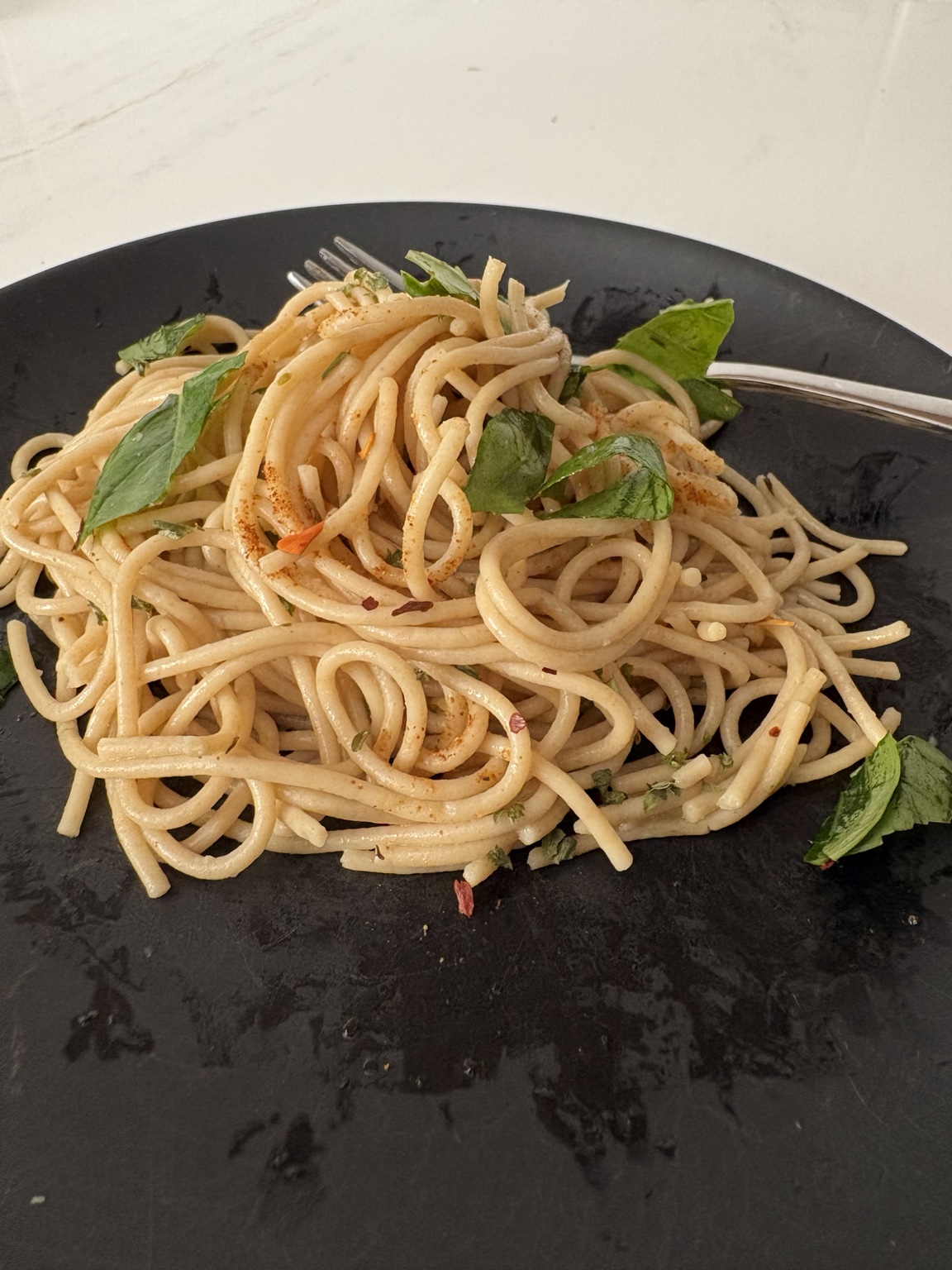 Whole grain pasta with fresh basil and herbs on a black plate