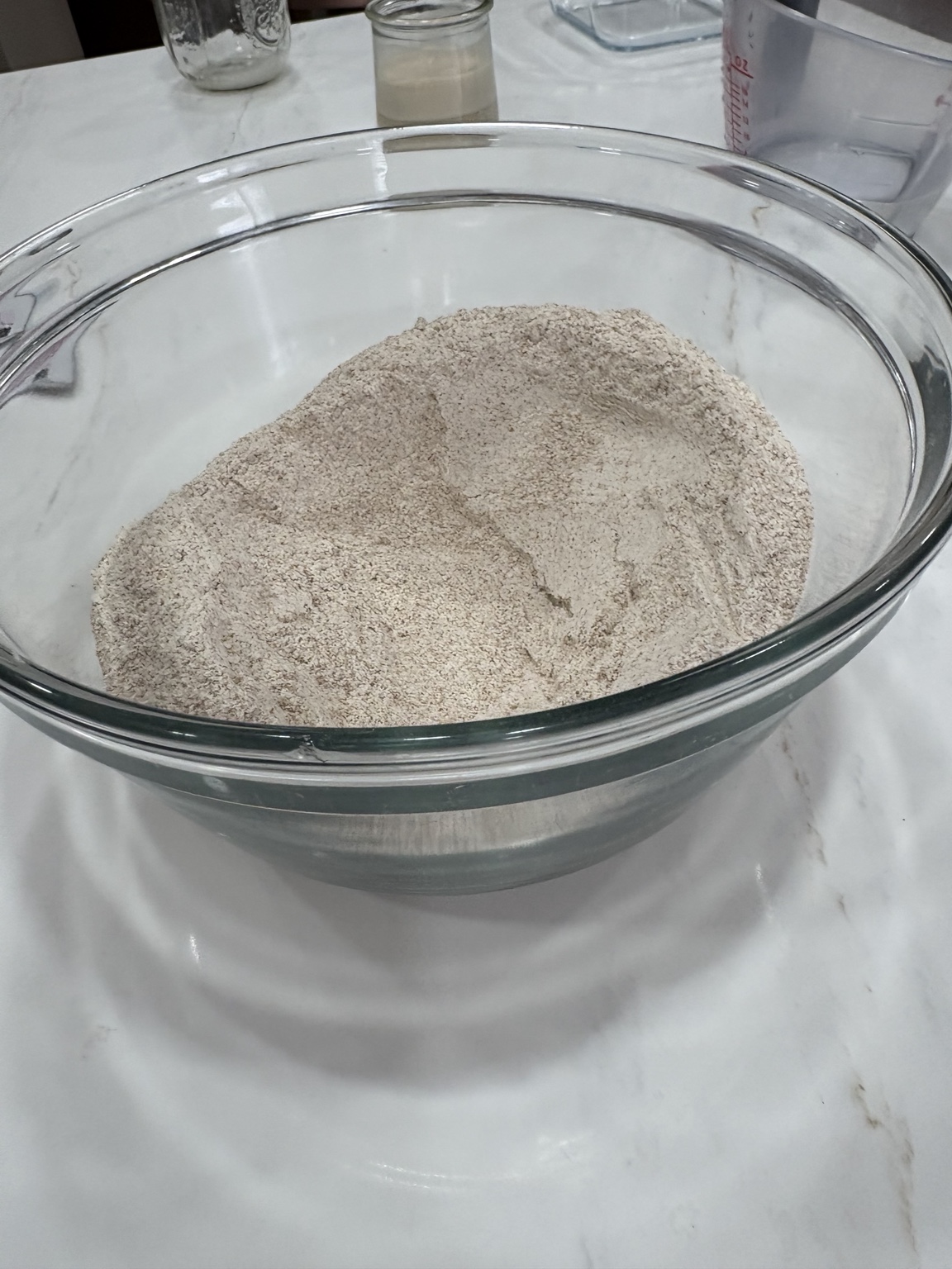 Whole wheat flour in a large clear glass mixing bowl with a well in the center