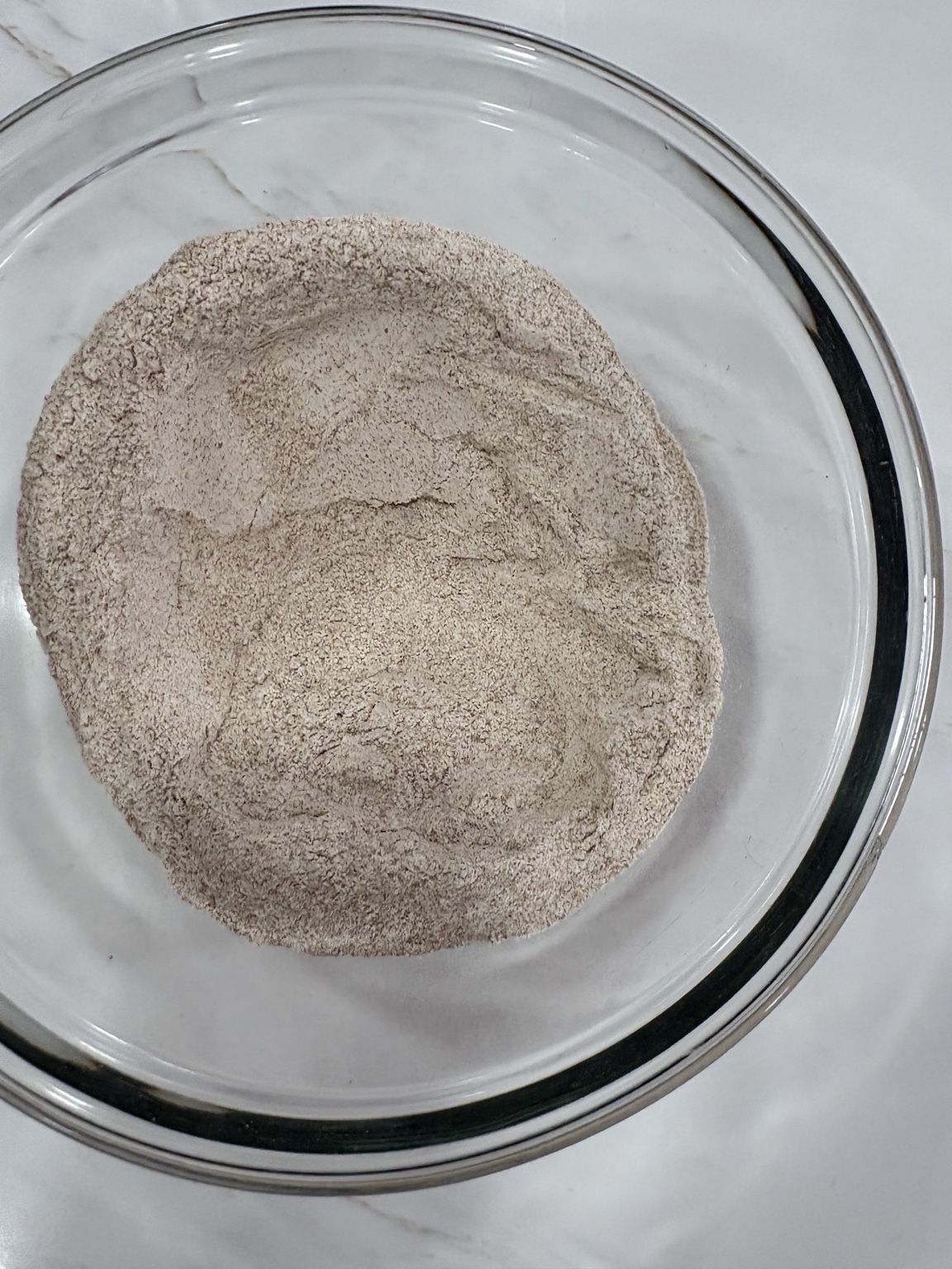 Overhead view of whole wheat flour with a well in a glass bowl